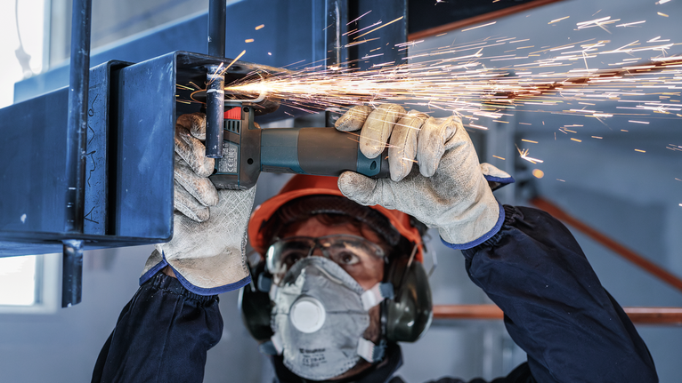 佩戴安全设备的人研磨金属，产生火花。