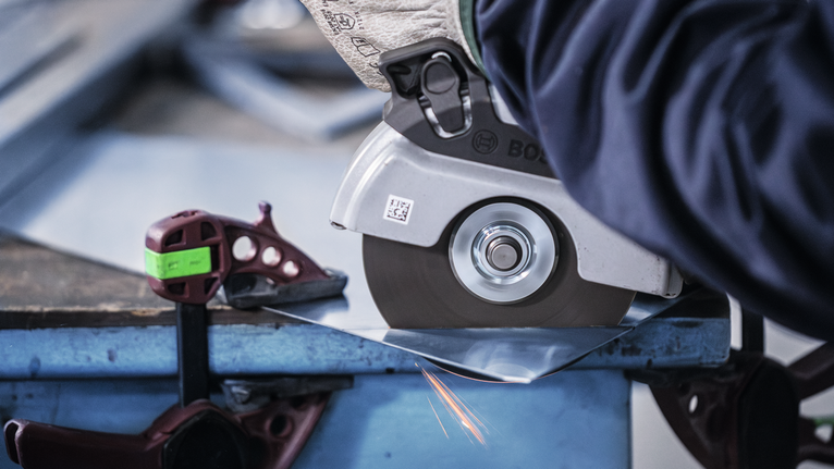 佩戴安全设备的人员使用角磨机切割金属板。