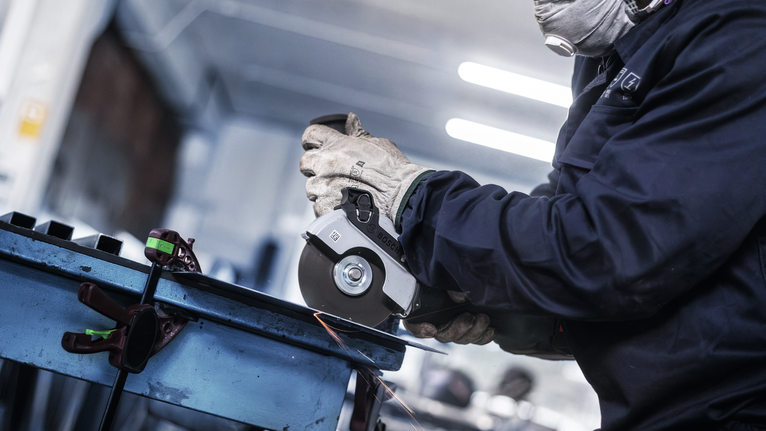 佩戴安全设备的人员使用角磨机研磨金属，产生火花。