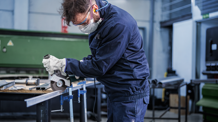 佩戴安全设备的人员使用角磨机切割金属棒。