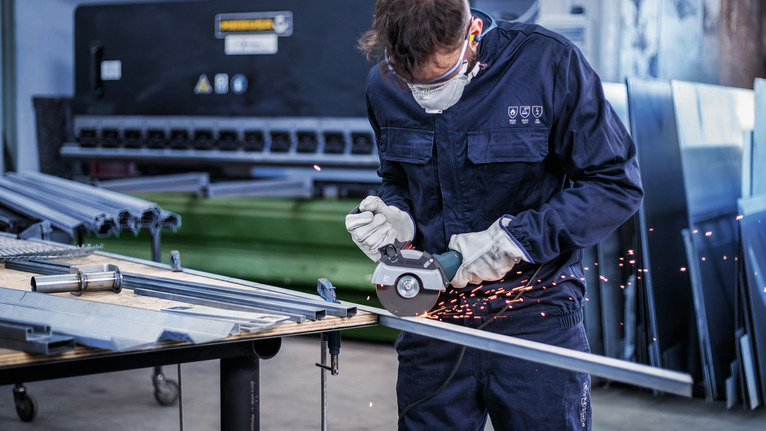 穿着安全设备的人员在车间使用切割工具切割金属棒。