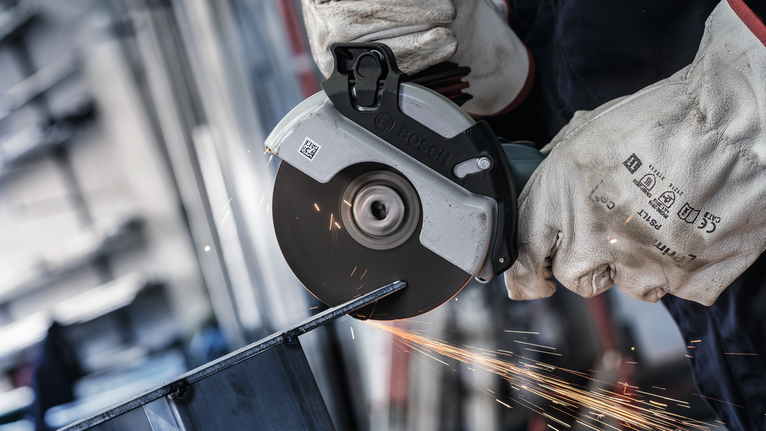 佩戴安全设备的人使用角磨机切割金属，产生火花。