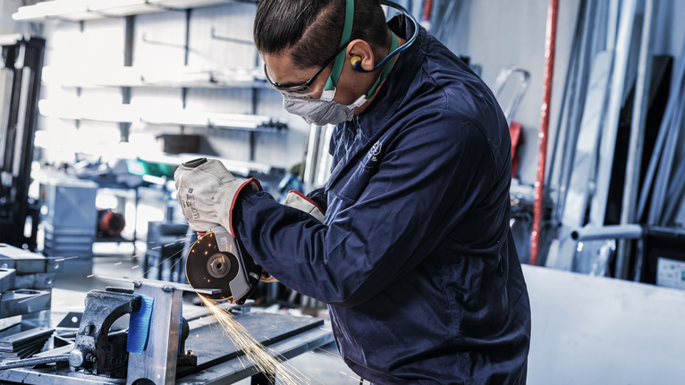 一名佩戴安全设备的人员在车间研磨金属，产生火花。