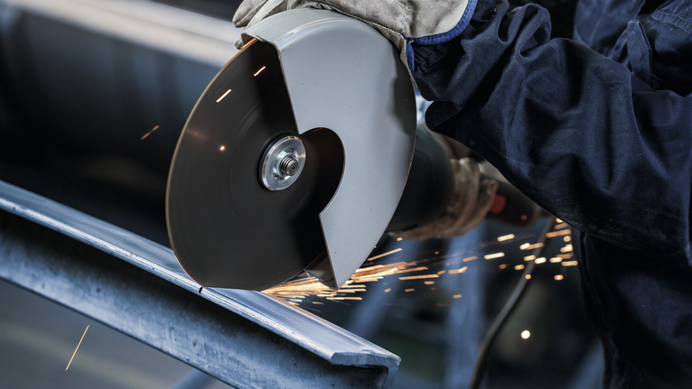 一名佩戴安全设备的人用角磨机切割金属，火花四溅。