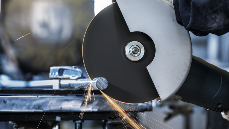 佩戴安全设备的人员使用大型角磨机切割金属，火花四溅。