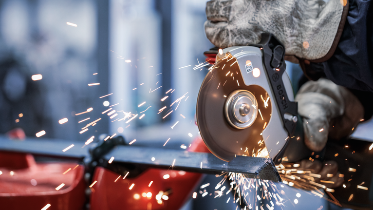 佩戴安全设备的人使用角磨机切割金属，产生火花。