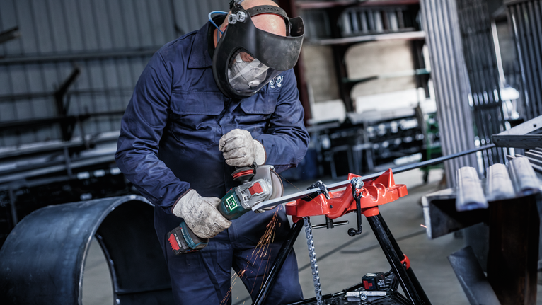 一名佩戴安全设备的人使用角磨机切割金属，产生火花。