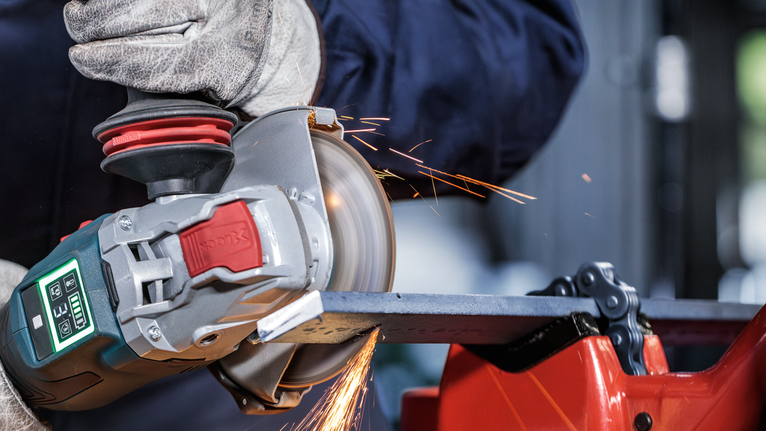 一名佩戴安全设备的人用角磨机打磨金属，产生火花。