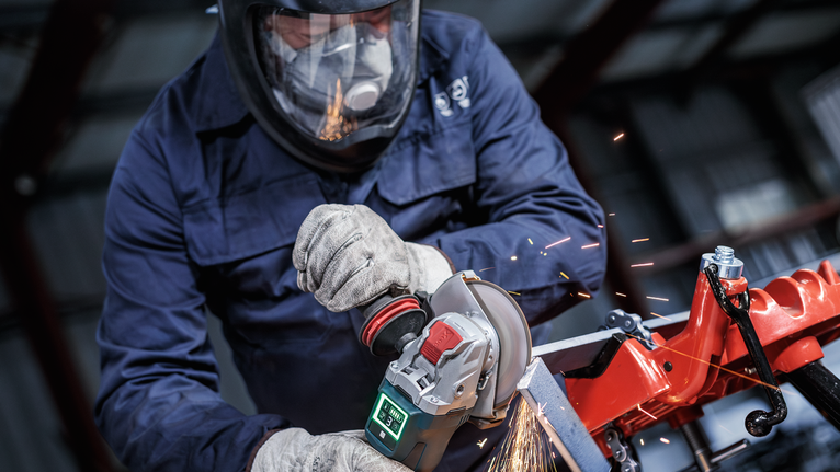 一名佩戴安全设备的人正在研磨金属，产生火花。