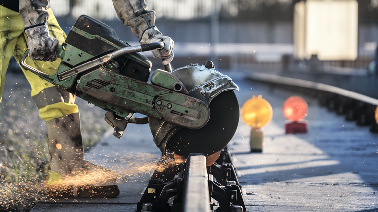 佩戴安全设备的人用圆锯切割铁轨，火花四溅。