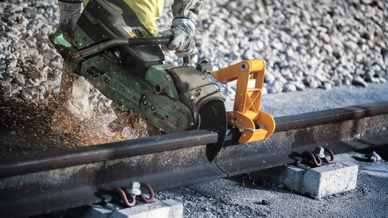 一名佩戴安全设备的人正在用电锯切割铁轨。