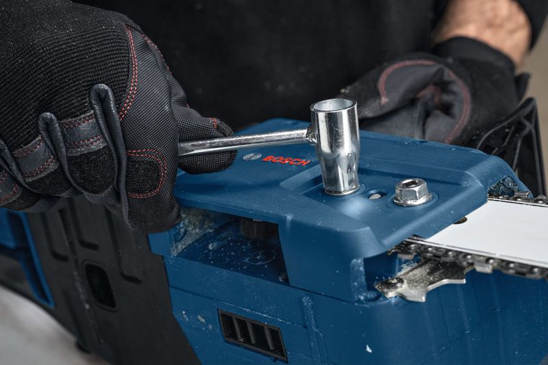 一名佩戴安全设备的人正在用扳手调整无绳电锯。.