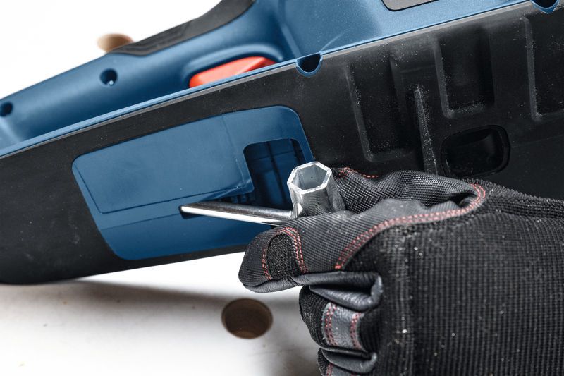 一名佩戴安全设备的人使用扳手调整无绳电锯。.