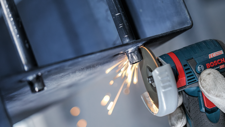 一名佩戴安全设备的人正在研磨金属梁，产生火花。