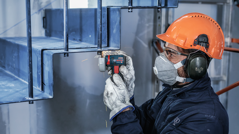 一名佩戴安全设备的人正在用电动工具打磨金属楼梯。