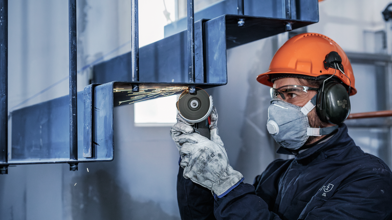 一名佩戴安全设备的人正在研磨金属梁，产生火花。