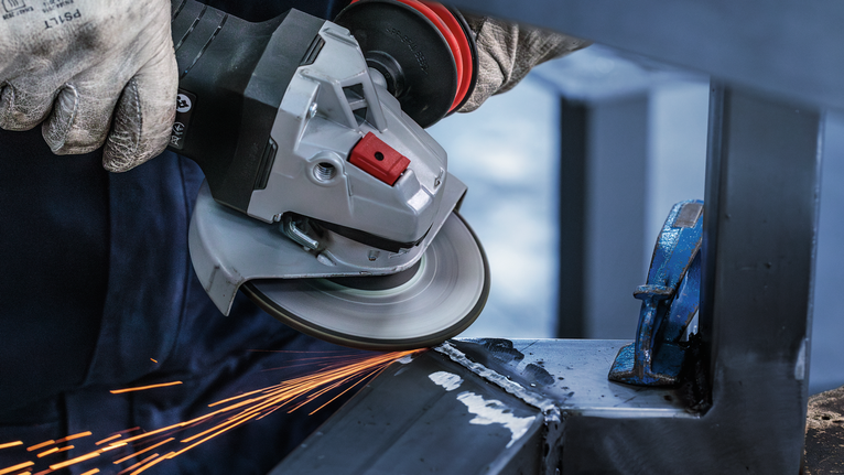 一名佩戴安全设备的人正在研磨金属，产生火花。