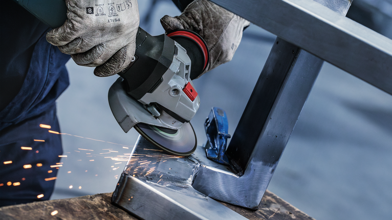 一名佩戴安全设备的人正在研磨金属框架，火花四溅。