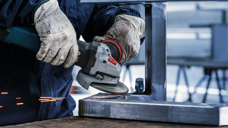 一名佩戴安全设备的人员正在用角磨机打磨金属梁。