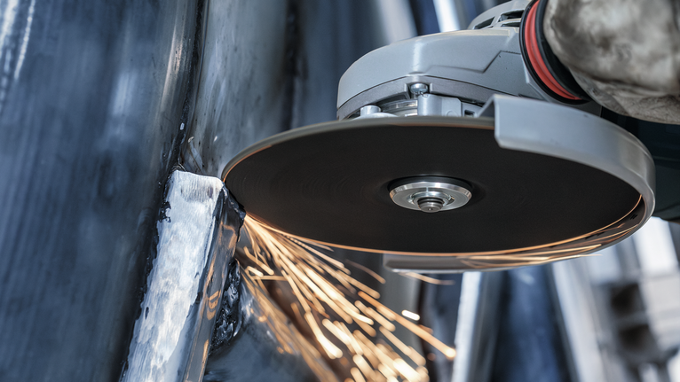 佩戴安全设备的人使用角磨机切割金属，产生火花。