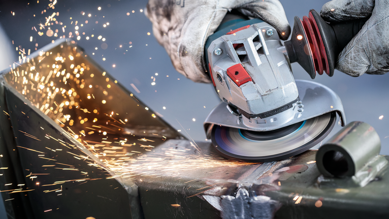 佩戴安全设备的人研磨金属，产生明亮的火花。