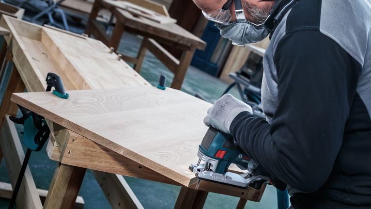 佩戴安全设备的人员使用曲线锯切割木板。