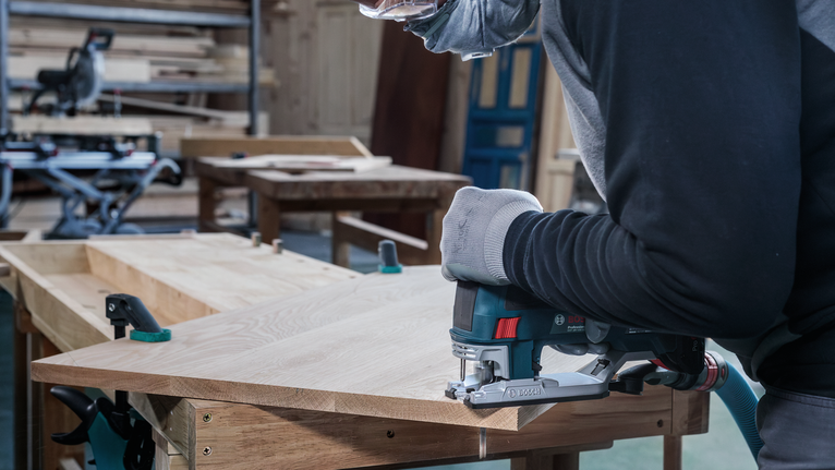 一名佩戴安全设备的工人在车间用曲线锯切割木材。