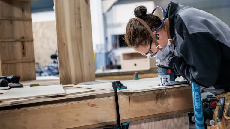 一名佩戴安全设备的人员在木板上使用木工工具。