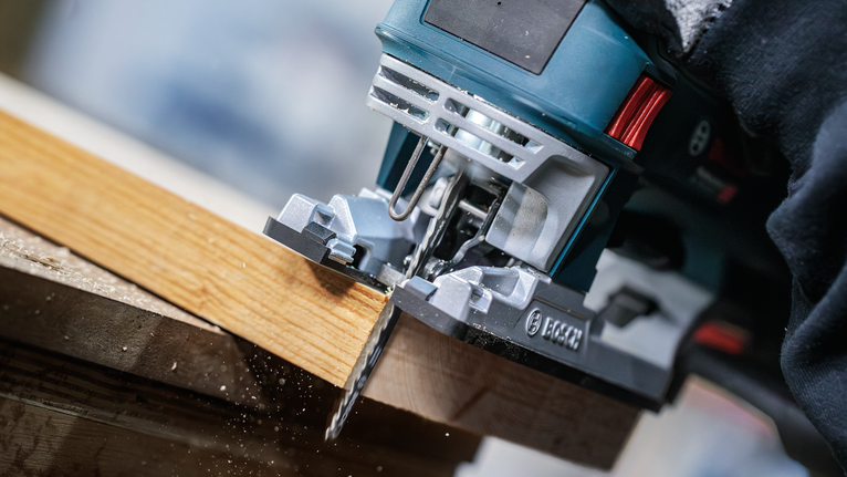 一名佩戴安全设备的人使用曲线锯切割木板。