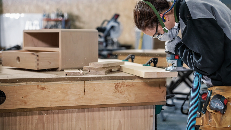 佩戴安全设备的人员使用电动工具在工作台上塑造木板。