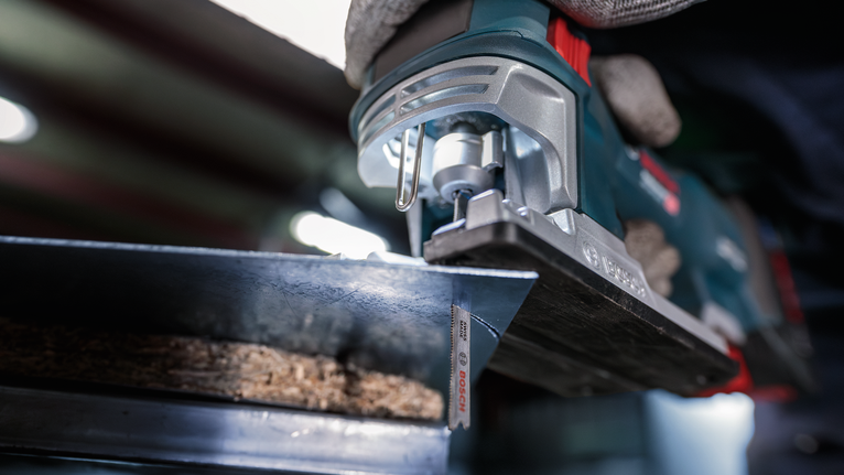 佩戴安全设备的人用曲线锯切割木材。