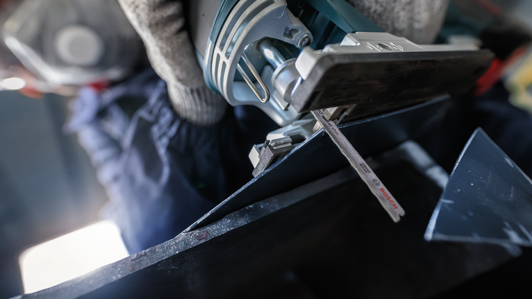 佩戴安全设备的人用曲线锯切割金属。
