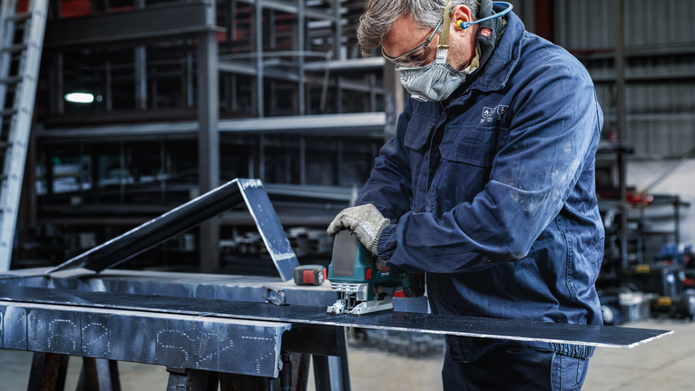 一名佩戴安全设备的人员使用电动工具切割金属板。