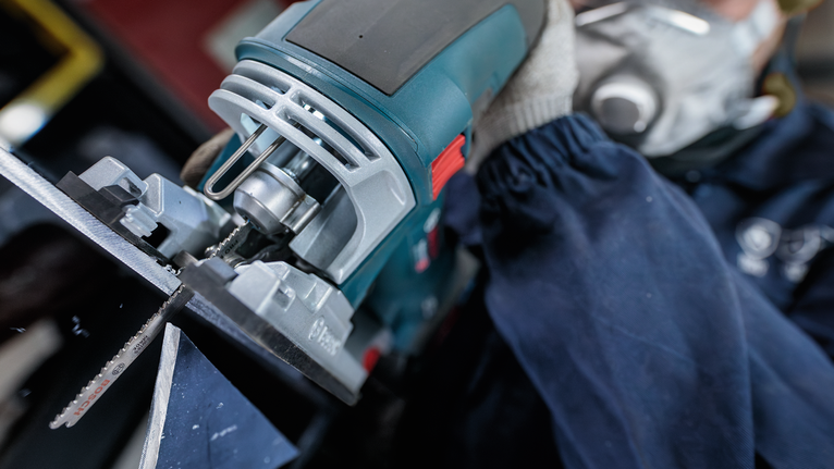 佩戴安全设备的人使用曲线锯切割金属。