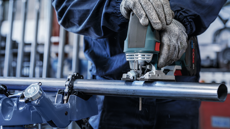 佩戴安全设备的人员使用曲线锯切割金属管。