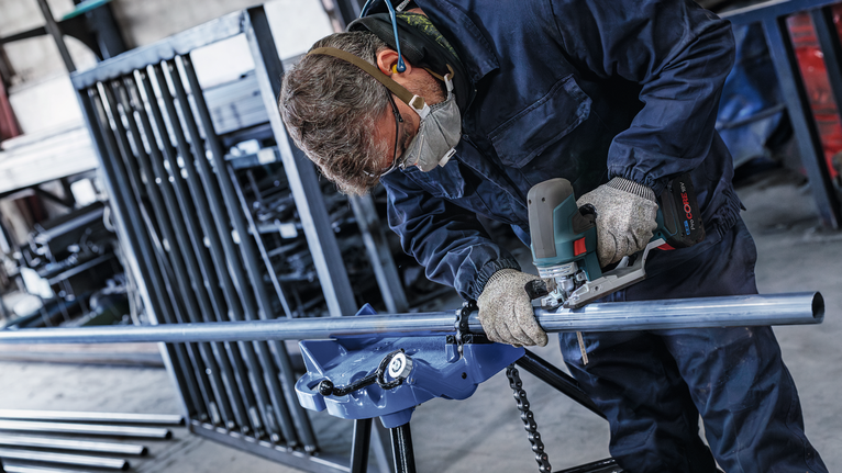 一名佩戴安全设备的人员在工业车间内打磨金属管道。