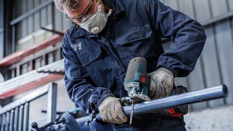 佩戴安全设备的人员用曲线锯切割金属管。