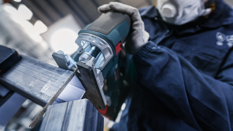 一名佩戴安全设备的人员使用往复锯切割金属梁。