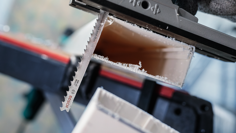 一名佩戴安全设备的人用曲线锯刀片切割塑料管。