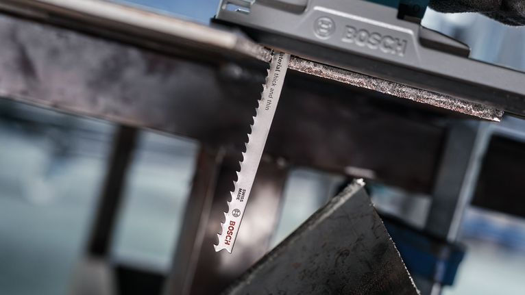 佩戴安全设备的人使用曲线锯切割金属板。