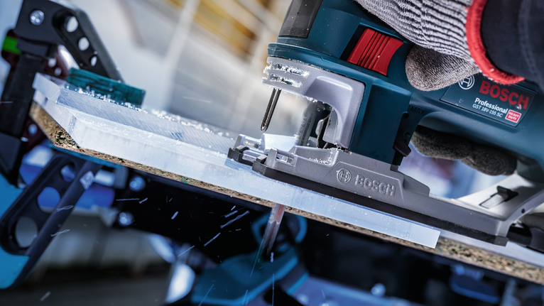 佩戴安全设备的人员用曲线锯切割塑料片。