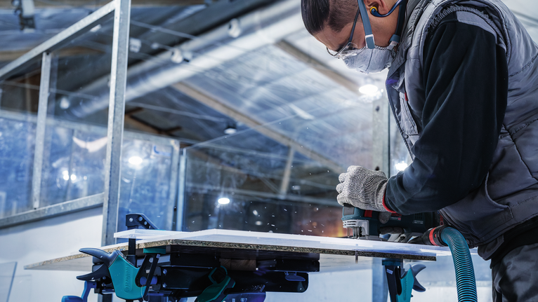 一名佩戴安全设备的人员使用电动工具切割木板。