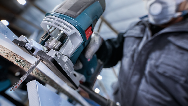 一名佩戴安全设备的人使用曲线锯切割一块材料。