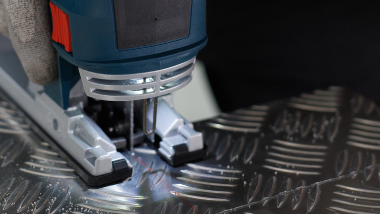 佩戴安全设备的人员操作曲线锯切割有图案的金属板。