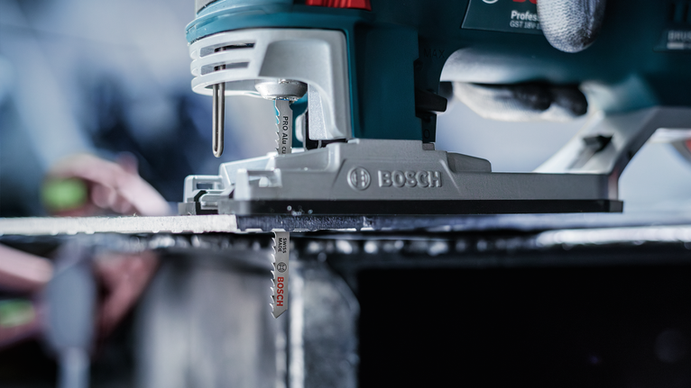 佩戴安全设备的人员引导曲线锯切割金属板。