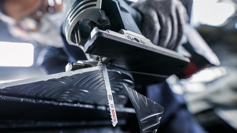 一名佩戴安全设备的人用曲线锯切割有图案的金属。