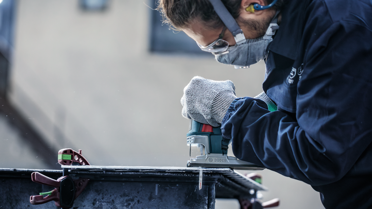 佩戴安全设备的人员使用曲线锯切割金属板。