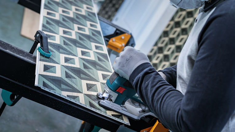 佩戴安全设备的人员用手持锯切割有图案的木板。