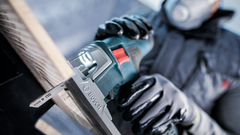 佩戴安全设备的人员使用往复锯切割木板。