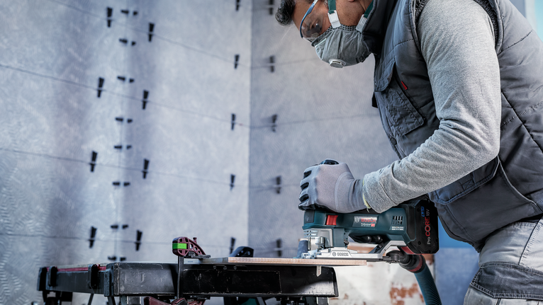 一名佩戴安全设备的人员使用电锯在工作台上切割木材。